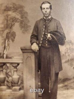 CDV soldier wearing frock coat, holding slouch hat. Dark trousers Cooperstown NY